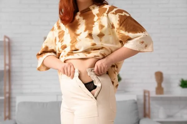 Image of woman trying to do her trousers up after pregnancy weight gain St Neots