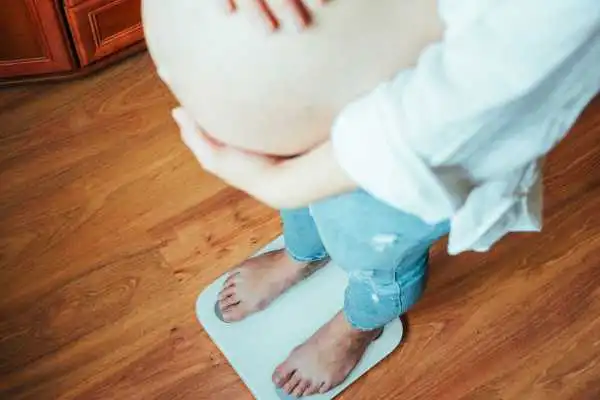 Image of woman weighing herself and experiencing weight gain through pregnancy St Neots